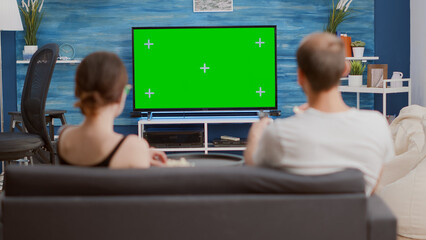 Static tripod shot of couple having a snack while looking at green screen tv watching a movie and...