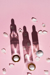 Bottles of cosmetic product cast shadows on a pink background. Top view, vertical image.