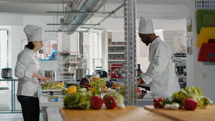 Man and woman cooking organic meal with celery and vegetables, doing gourmet dish preparations in kitchen, Professional team of authentic chefs making fresh food with gastronomic recipe.