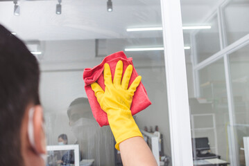 A man wearing yellow gloves wipes clean the surface of an office glass window with a red microfiber...