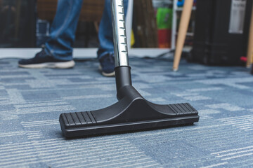 A man cleans the carpet flooring of an office with a vacuum cleaner with an attached floor sweeper...