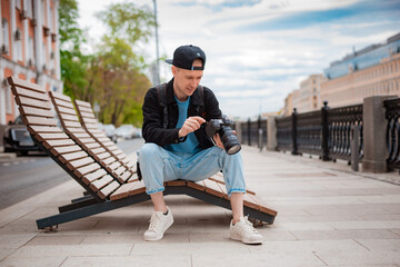 Young focused millenial male photographer tries to make photo on professional camera outdoors