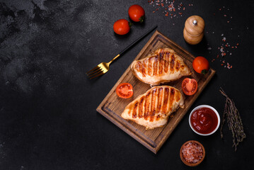 Delicious fresh grilled chicken fillet with spices and herbs on a dark concrete background