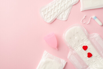 Top view photo of panty liners menstrual cup sanitary napkins with red hearts and tampons on isolated pastel pink background