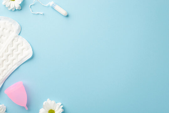 Top view photo of camomile flower buds sanitary napkins pink menstrual cup and tampon on isolated pastel blue background with copyspace