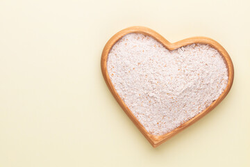 Wheat flour in a wooden heart shape bowl on a pastel background.