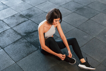 Sitting on the ground. Woman in sportive clothes with slim body type is in the gym