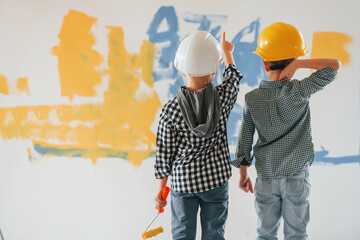 In hard hats. Two boys painting walls in the domestic room