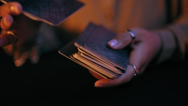 Close-up hands of mysterious fortuneteller shuffling tarot cards, magic ritual