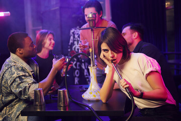 Woman smoking hookah. Group of friends having fun in the night club together