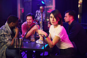 Talking with each other when sitting by the table with hookah. Group of friends having fun in the night club together