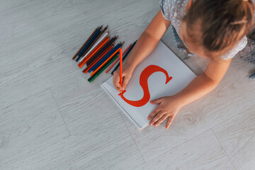Top view of little girl that writing s letter when laying down on the ground at home
