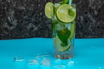 Glass of Mojito cocktail with mint and lime ice cubes on a black board with fresh limes. Sparkling refreshing water. Place for text