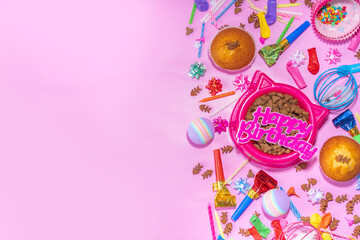 Pet cat happy birthday background with set different cats and kitty snack, food and toys, cat muzzle shape bowl, birthday cupcakes with happy birthday candles, accessories. Flatlay on pink background