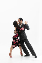 Fototapeta na wymiar Couple of professional tango dancers in elegant suit and flowery print dress pose in a dancing movement on white background. Handsome man and woman dance looking eye to eye.