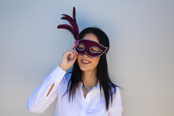Young and beautiful brunette woman with a purple carnival mask with rhinestones and feathers on a...