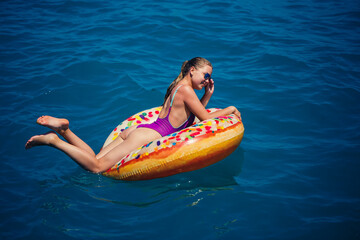 Beautiful happy young woman in a swimsuit with an inflatable ring relaxing in the blue sea. Sunny day, seaside vacation, tourism