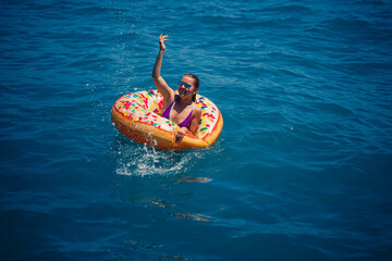 Beautiful young woman in the sea swims on an inflatable ring and has fun on vacation. Girl in a bright swimsuit at the sea under the sunlight