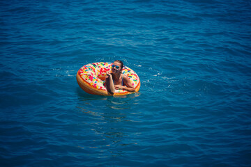 Beautiful young woman in the sea swims on an inflatable ring and has fun on vacation. Girl in a bright swimsuit at the sea under the sunlight