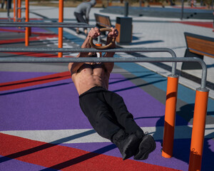 Shirtless man doing horizontal balance on parallel bars at sports ground. 