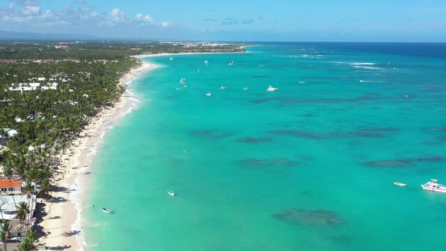 Tropical seashore with resorts, palm trees and caribbean sea with floating boats and people having fun doing paraseiling. Travel destinations. Dominican Republic. Aerial view