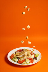 Caesar salad with chicken sprinkled with breadcrumbs in a plate with an orange background