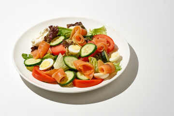 Salad with salmon, cucumber, tomatoes and cream cheese on a white plate on a white background
