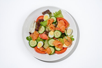 Salad with salmon, cucumber, tomatoes and cream cheese on a white plate on a white background