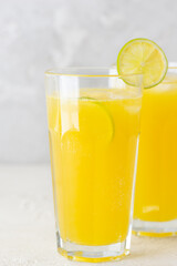 Fresh orange juice with ice and lime slices in glasses on a light background.