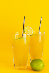 Freshly squeezed orange juice with ice and lime slices in glasses on a yellow background.