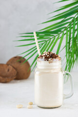 Vegan milkshake with nuts and caramel in a mug on the background of a palm branch and coconut.