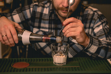 Bartender pouring coffee liqueur into glass with cream while preparing cocktail White Russian