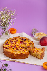 Homemade peach pie with almond cream on the lilac background. Slice of pie tart. Delicious homemade cakes. Selective focus. Image with copy space. Open pie with peaches and frangipane.