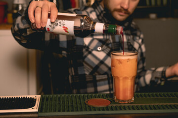 Fototapeta na wymiar Bartender preparing Tequila Sunrise cocktail, adding pomegranate syrup into glass with drink