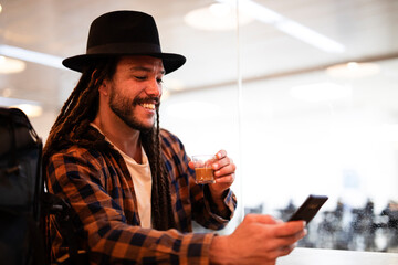Young hipster man using his smartphone while drinking coffee. Smiling man sitting in a coffeehouse and drinking coffee.