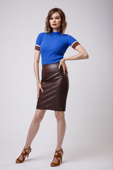 High fashion photo of a beautiful elegant young woman in a pretty leather brown skirt, blue top posing on white background. Slim figure, hairstyle, studio shot.