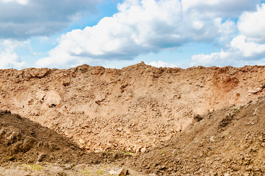 A pile of soil dug out of a trench against a blue cloudy sky. Earthworks at the construction site.