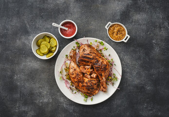 Two chicken legs grilled with garlic on a white plate. Served with mustard, ketchup and pickles, top view, flat lay