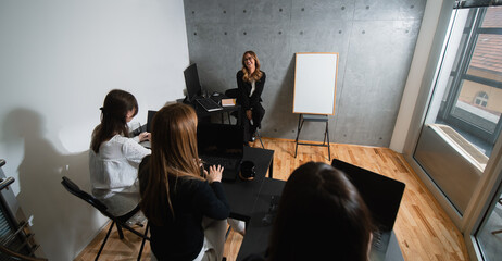 An enthusiastic, happy, formal dressed caucasian female trainer lectures seminars to female participants. Associates are unrecognizable and turned at a trainer. A trainer wears eyeglasses. 