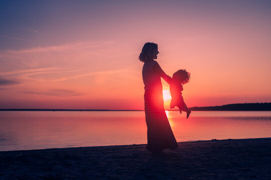 Happy family moment. Silhouette of mom spinning her baby on a sunset background. Beautiful landscape. Love and motherhood. Freedom. Childhood. Sisters relationship. International woman day. Sea trip