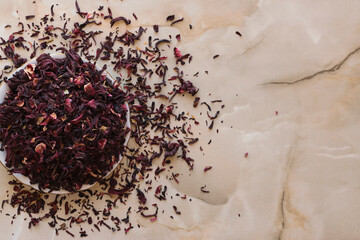 Dry hibiscus tea in a bowl. Dried hibiscus calyces, herbal tea made of crimson and deep magenta-colored sepals of the roselle flower, in the bowl on the table, top view.