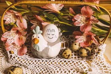 Easter basket with quail eggs and pink flowers. Decorative chicken with egg with a smile. Pink alstroemerias around.