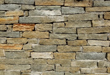 Exterior stone wall made of rock  bricks. Colors are gray, brown, green and orange. Background and texture.
