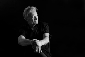 low key portrait of a senior man sitting a chair looking at away on black background