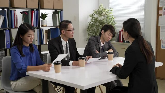 three asian hr managers holding cv are nodding head and looking at each other while interviewing a female job candidate in the meeting room