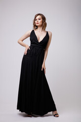 Fototapeta premium High fashion photo of a beautiful elegant young woman in a pretty black evening party dress with a deep neckline posing on white background. Slim figure, hairstyle, studio shot. 