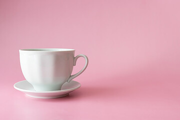 A ceramic white cup on a small saucer on a pink table. Light pink background, text space