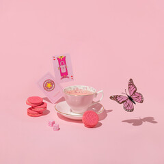 Spring or summer creative layout with cup of tea, pink sandwich cookies, dices, playing cards and butterfly on pastel pink background.  80s or 90s retro fashion aesthetic concept. Romantic food idea.