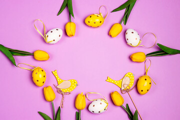 Easter frame with decorative eggs, birds and yellow tulips on purple background.