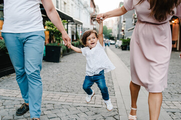 Young happy family: father, daughter, mother throws a baby during a walk the streets near ancient...